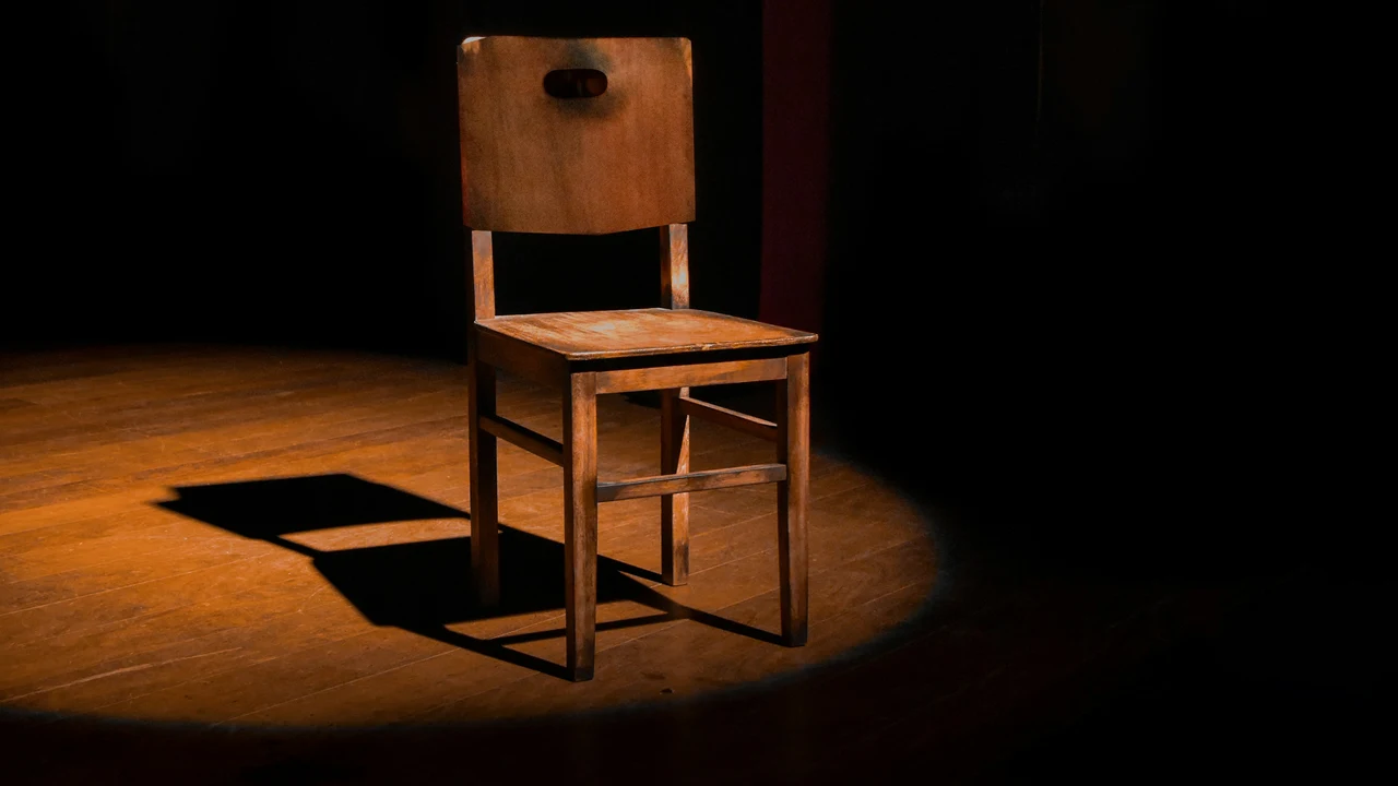 Empty chair under a spotlight on a dark stage, representing the weight of contestable decisions