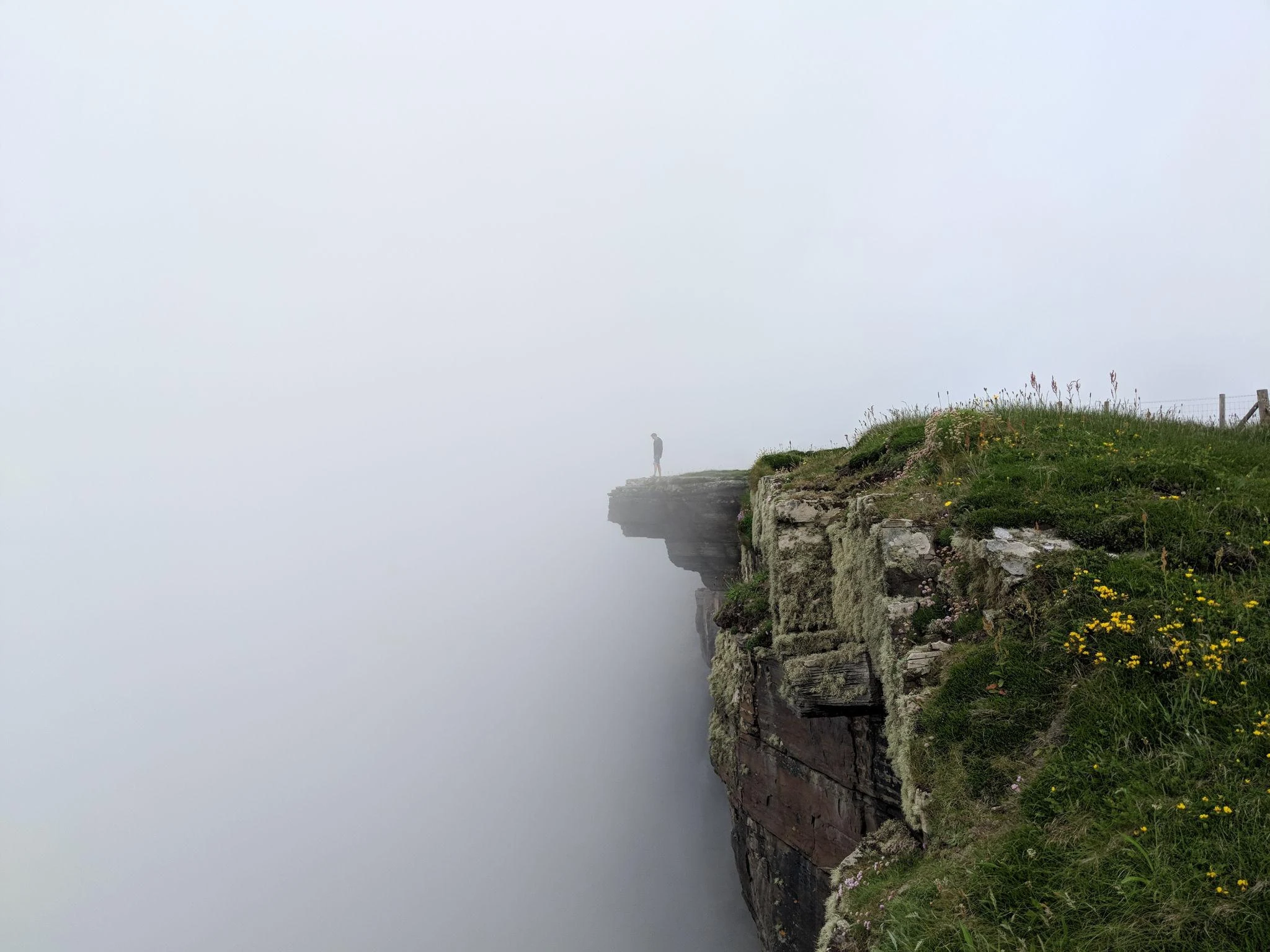 Figure standing at the edge of a cliff in fog, representing the irreversibility of consequential decisions